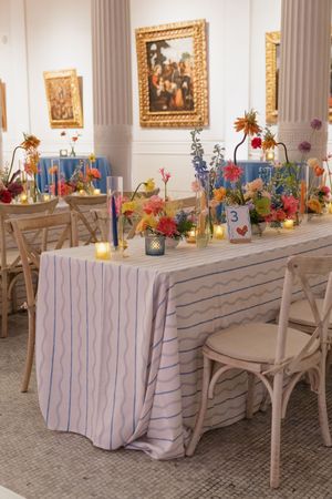 Elegant wedding reception table with colorful floral centerpieces, candles, and striped linen in an art gallery venue.
