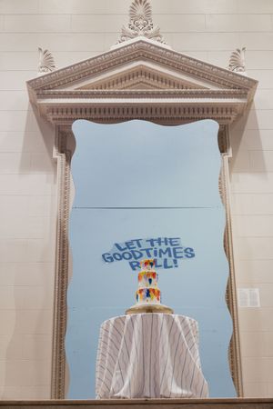 Elegant mirror with ornate frame reflects a tiered wedding cake and Let The Good Times Roll sign.
