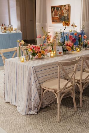 Elegant wedding reception table with striped linen, colorful florals, and candles in bright venue.