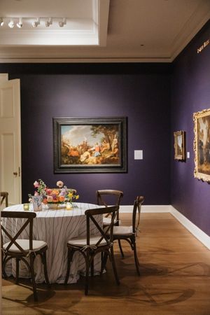Intimate wedding dinner table set in purple gallery room surrounded by classic oil paintings.