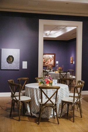 Elegant wedding reception tables with floral centerpieces set in a purple art museum gallery.