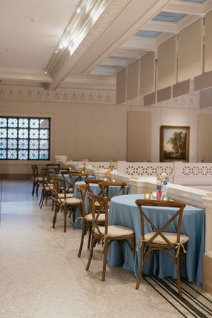Elegant wedding reception venue with blue tablecloths, wooden cross-back chairs, and ornate architectural details.