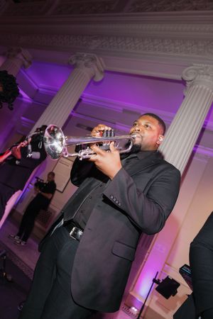 Trumpet musician performing in elegant white columned ballroom with purple lighting at wedding reception.