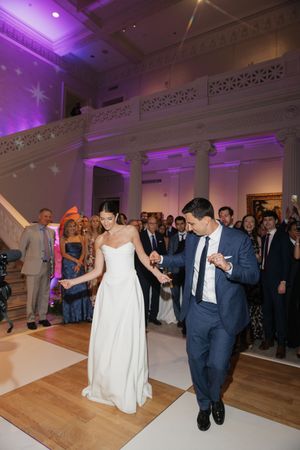 Bride and groom share first dance in elegant museum venue with purple uplighting and guests watching.
