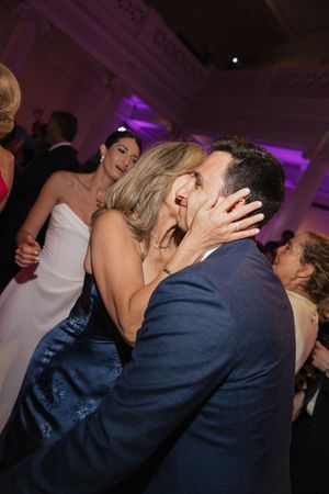 Emotional mother kisses her son the groom in a navy suit on the dance floor during wedding reception celebration.