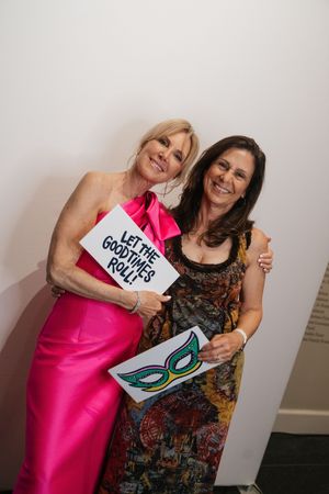 Two smiling women pose with fun photo booth props at a festive wedding reception.