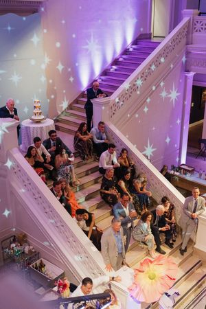 Wedding guests gather on grand staircase with purple uplighting and star projections at reception.