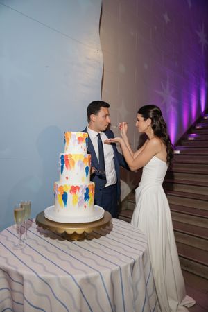 Bride and groom cutting colorful painted three-tier wedding cake at elegant reception venue.