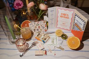Wedding reception table display with Corey and Michael programs, sticker sheets, citrus fruits, and cocktails.