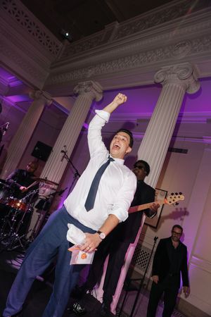 Man in white shirt and tie celebrates with fist raised at elegant wedding reception with live band.
