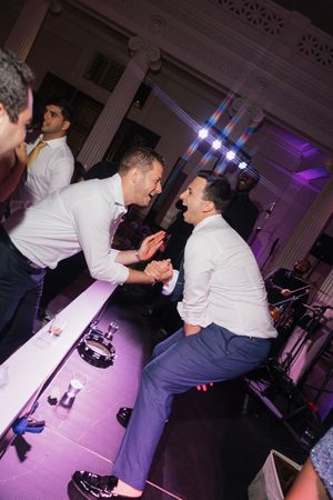 Guests dancing energetically on stage at lively wedding reception with purple lighting.