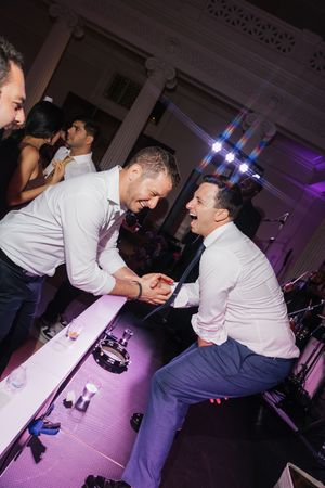 Two men laughing and celebrating together on the dance floor at a lively wedding reception.