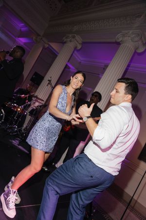 A couple dancing energetically at an elegant event venue with purple lighting and classical columns in the background.