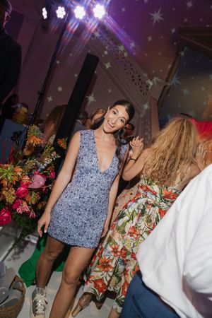 Bride in blue floral mini dress smiles while dancing among guests at a vibrant wedding after-party with star lighting.