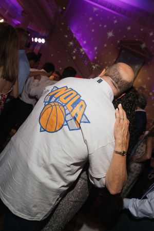 Guest wearing NOLA basketball t-shirt dances at vibrant wedding reception under purple lighting on dance floor.