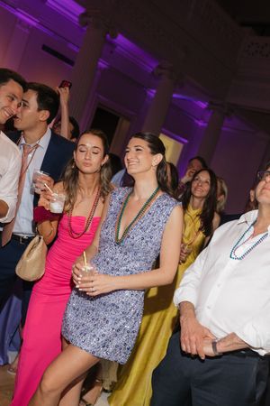 Guests wearing Mardi Gras beads dance and celebrate at lively indoor wedding reception with purple ambient lighting.