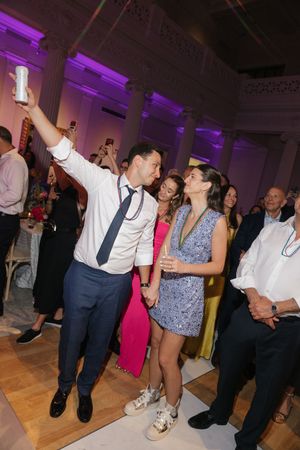 Groom takes selfie with bride in sparkly mini dress on dance floor during lively wedding reception.