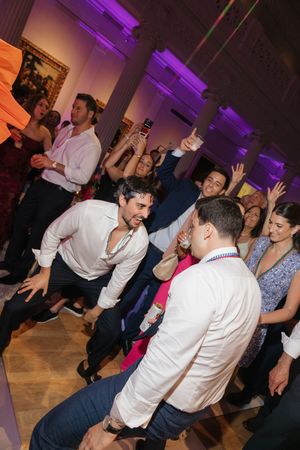 Guests dancing energetically at a lively wedding reception in a museum venue with purple lighting.