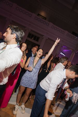 Excited wedding guest raises hand on crowded dance floor at lively evening reception celebration.