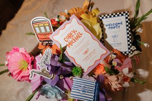 Colorful wedding welcome basket with floral arrangements, streetcar cutout, and personalized Corey and Michal invitation cards.
