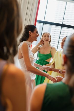 Bride in white dress laughing with bridesmaids in colorful green and yellow gowns before wedding.