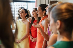 Bridesmaids in colorful dresses smile together during wedding preparations.
