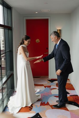 Emotional father-daughter first look moment with bride in white gown in colorful hotel corridor.