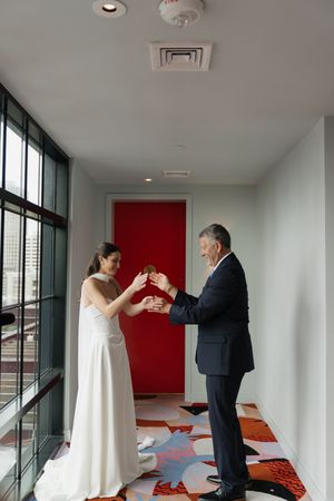 Bride and father sharing a champagne toast in a modern hotel hallway before the wedding ceremony.