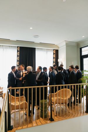 Groomsmen in navy suits gather and mingle in an elegant venue with gold railings and wicker chairs.