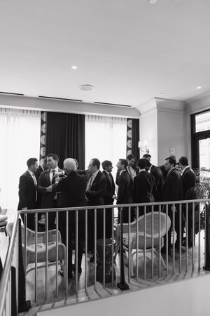 Black and white photo of groomsmen in suits gathered on a balcony before a wedding ceremony.