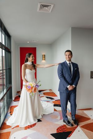 Bride in white gown touches groom's shoulder during first look moment in colorful patterned hallway.