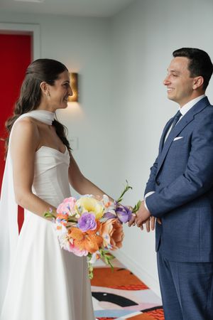 Bride and groom sharing joyful first look moment, bride holding vibrant colorful floral bouquet.