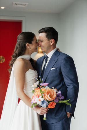 Bride and groom share an intimate moment holding a colorful floral bouquet during first look.