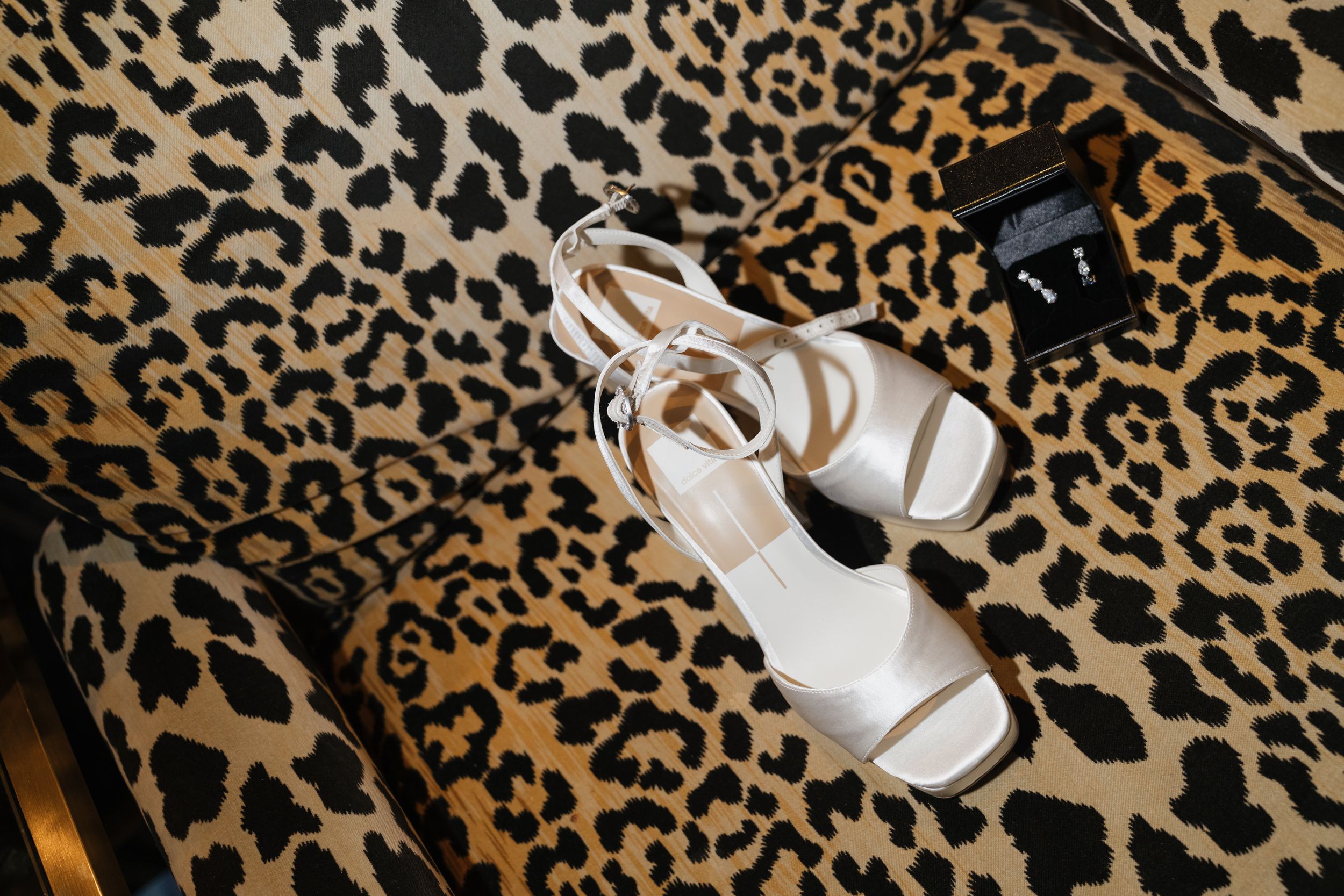 White strappy heeled sandals and earrings displayed on a leopard print chair.