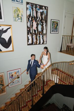Bride and groom descend elegant staircase adorned with colorful artwork, holding hands on their wedding day.