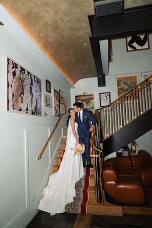 Bride and groom sharing a romantic kiss on a staircase in a stylishly decorated wedding venue interior.