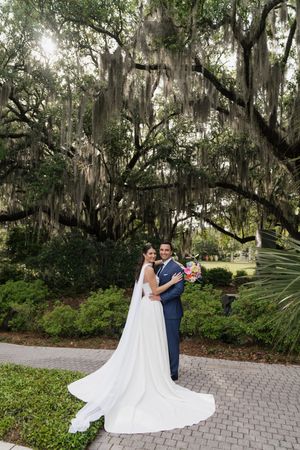 Bride and groom pose under Spanish moss-draped oak trees with long white wedding dress train.