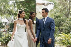 Bride in white gown and groom in navy suit hold hands near a mirrored altar with officiant.