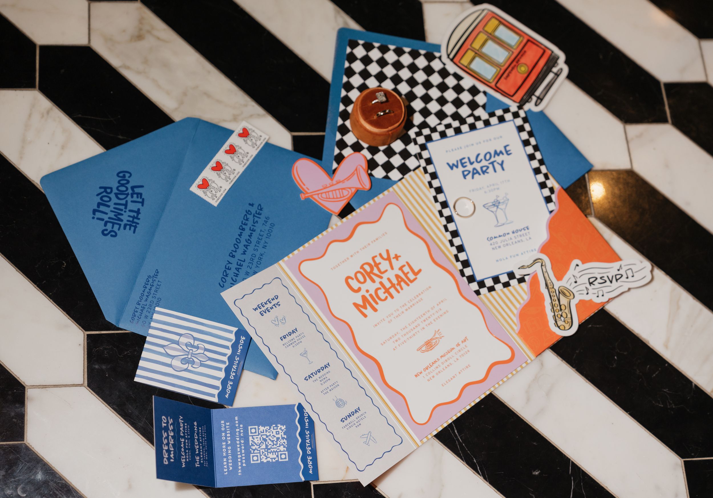 Colorful wedding stationery suite with checkered envelope, welcome party card, and blue invitations on black and white floor.