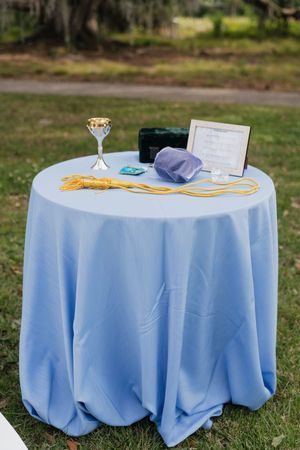 Blue tablecloth-covered ceremony table with ketubah, kiddush cup, and gold rope for Jewish wedding.