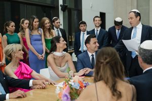 Jewish wedding ketubah signing ceremony with bride, groom, and guests gathered around a wooden table.