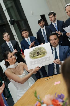 Bride and groom proudly display illustrated ketubah to guests during Jewish wedding signing ceremony.