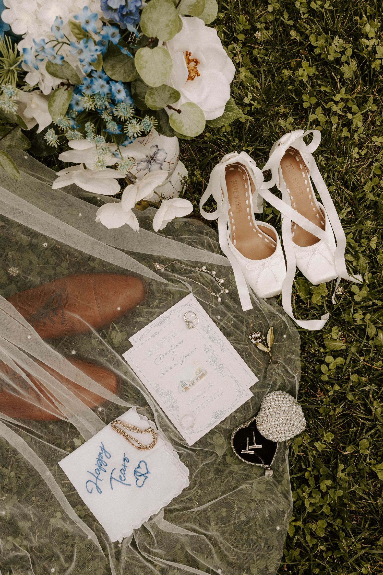Bride and groom holding hands walking toward a white barn wedding venue with a fountain and lush greenery.