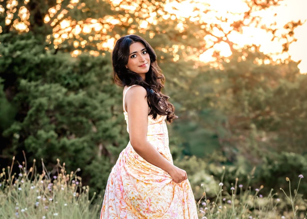 Young woman in floral maxi skirt posing outdoors at golden hour with lush green trees in background.