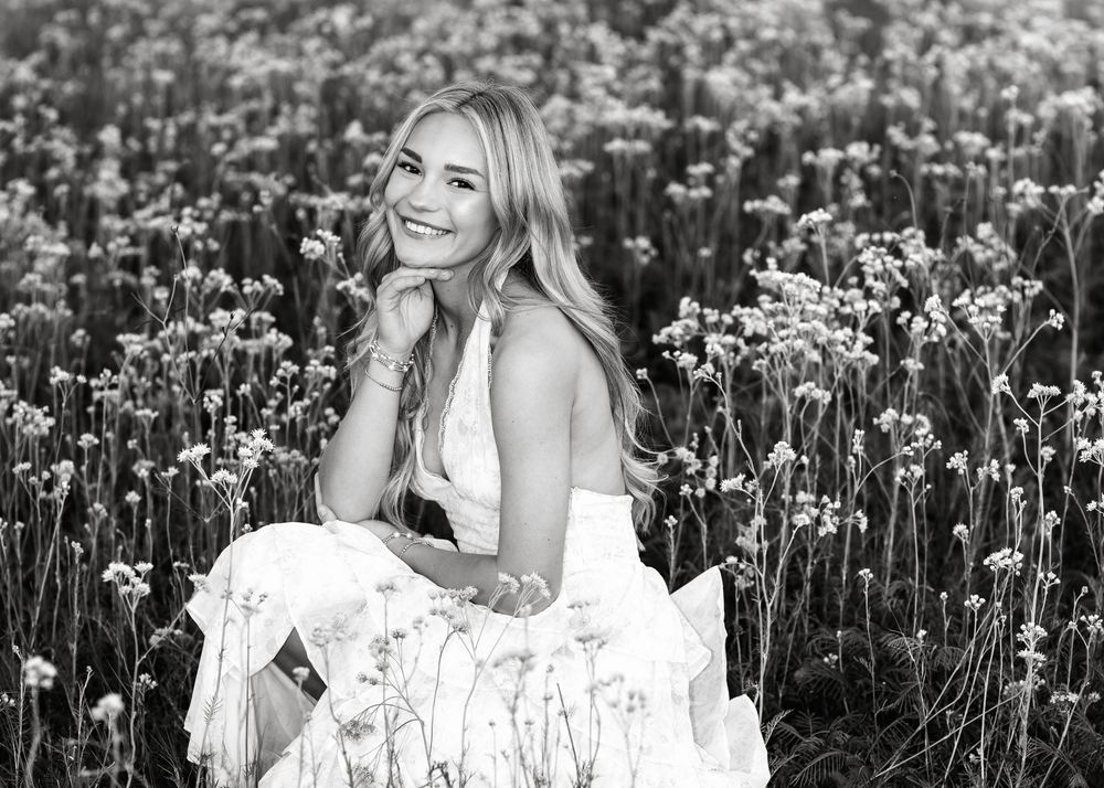 Young woman smiling in a wildflower field, wearing a white dress, black and white photo.
