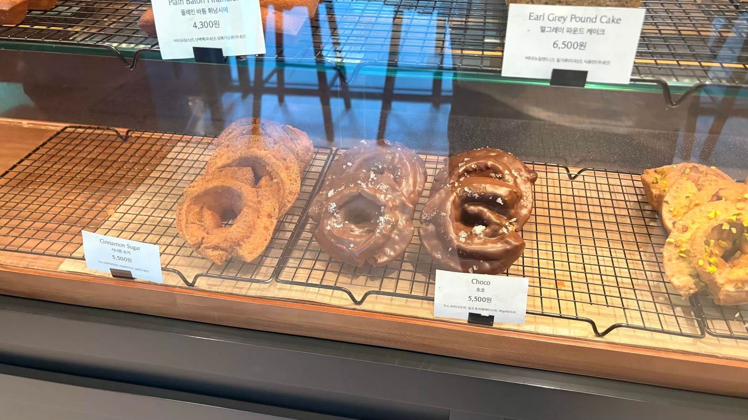 Bakery display case featuring three gourmet pretzels and pretzel cakes on wire racks with price tags.