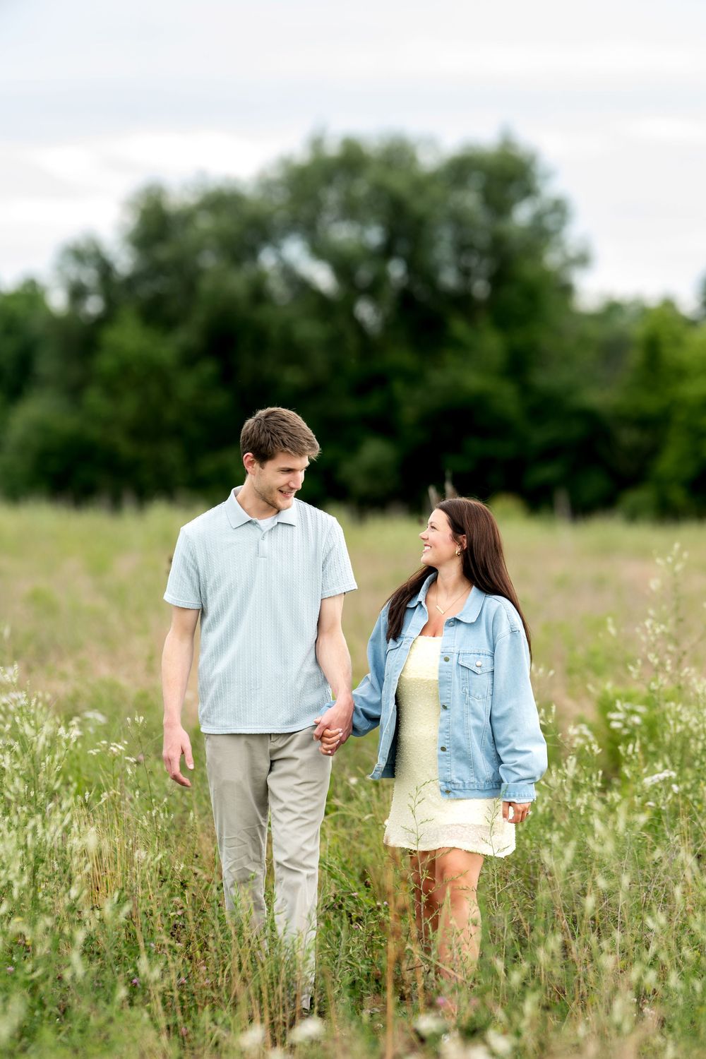 A happy couple holds hands and smiles at each other while strolling through a beautiful wildflower meadow.
