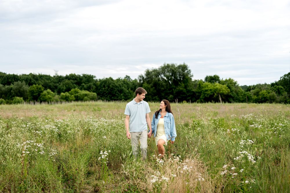 A couple walks hand in hand through a scenic wildflower meadow.