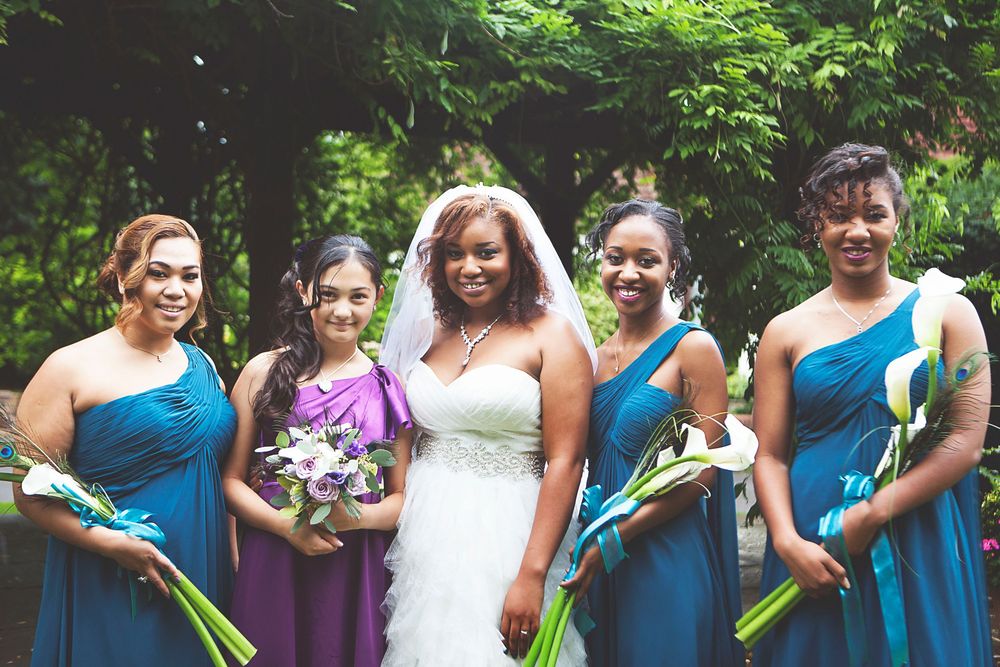 Bride in white gown with bridesmaids in teal and purple dresses holding floral bouquets outdoors. At Oaks farm wedding venue in Surrey.