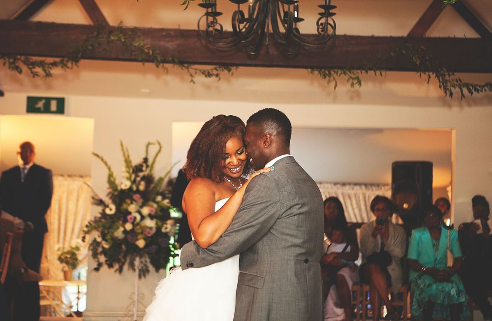 A joyful bride and groom share their first dance at an elegant wedding reception with floral arrangements. At Oaks farm wedding venue.